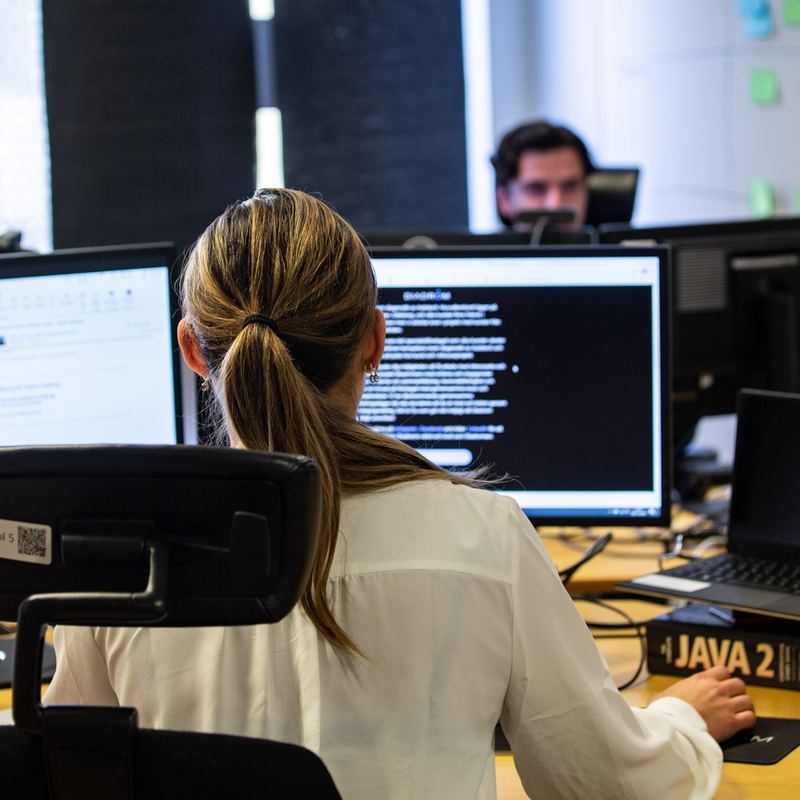 Two Diadrom engineers working at adjacent desks, one reviewing code on a large monitor